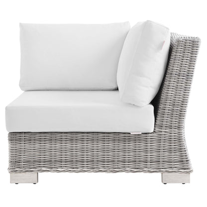 Light gray wicker outdoor corner chair with white cushions for contemporary patio seating.