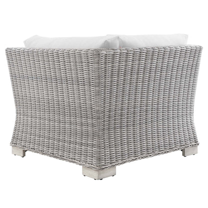 Light gray woven wicker outdoor corner chair with white cushions and pale wooden feet.