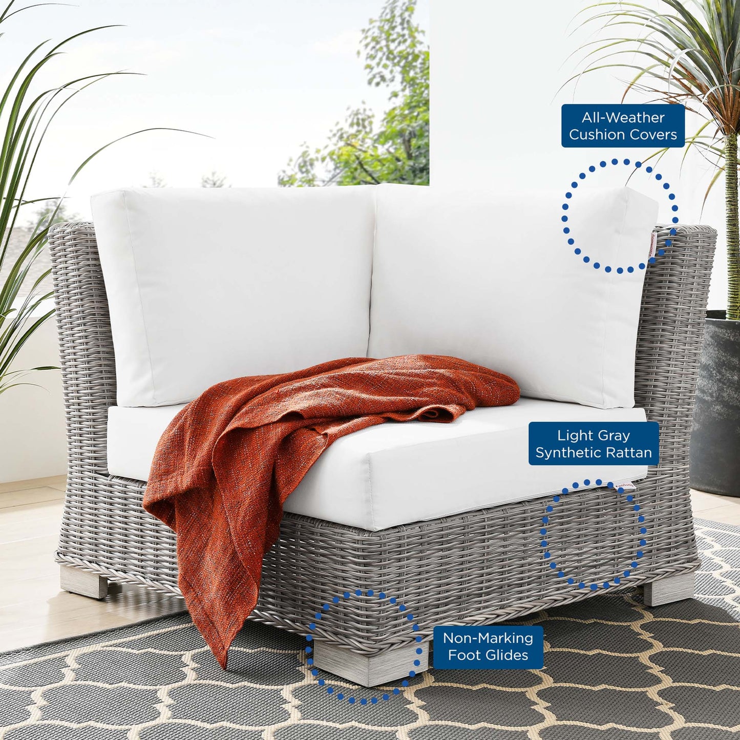 Outdoor light gray synthetic rattan corner chair with white cushions and an orange throw for patio lounging.