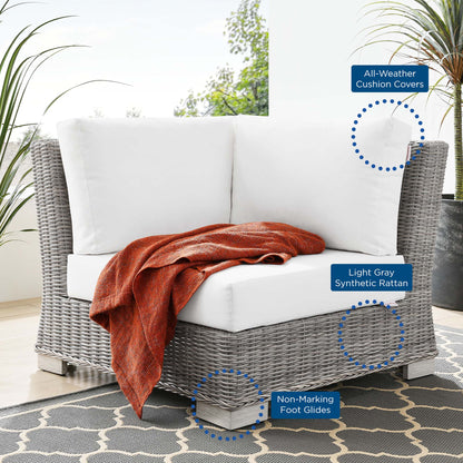 Outdoor light gray synthetic rattan corner chair with white cushions and an orange throw for patio lounging.
