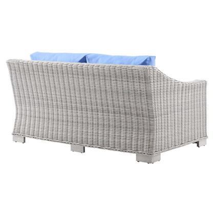 Light gray wicker outdoor loveseat with curved sides and blue cushions, square block feet.
