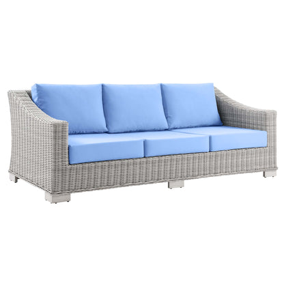 Gray wicker outdoor sofa with light blue cushions, curved arms, three-seat design for patio lounging.