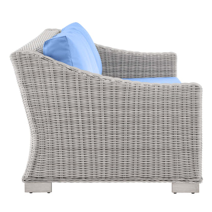 Light gray wicker outdoor sofa with light blue cushions, curved back and arms, square base—patio lounge seating.