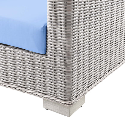 Gray woven synthetic rattan outdoor sofa with blue cushion and light wood base