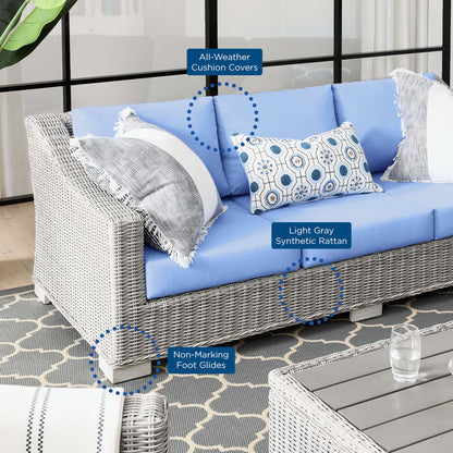 Outdoor wicker sofa with light-blue cushions, gray synthetic rattan, all-weather cushion covers, and non-marking foot glides.