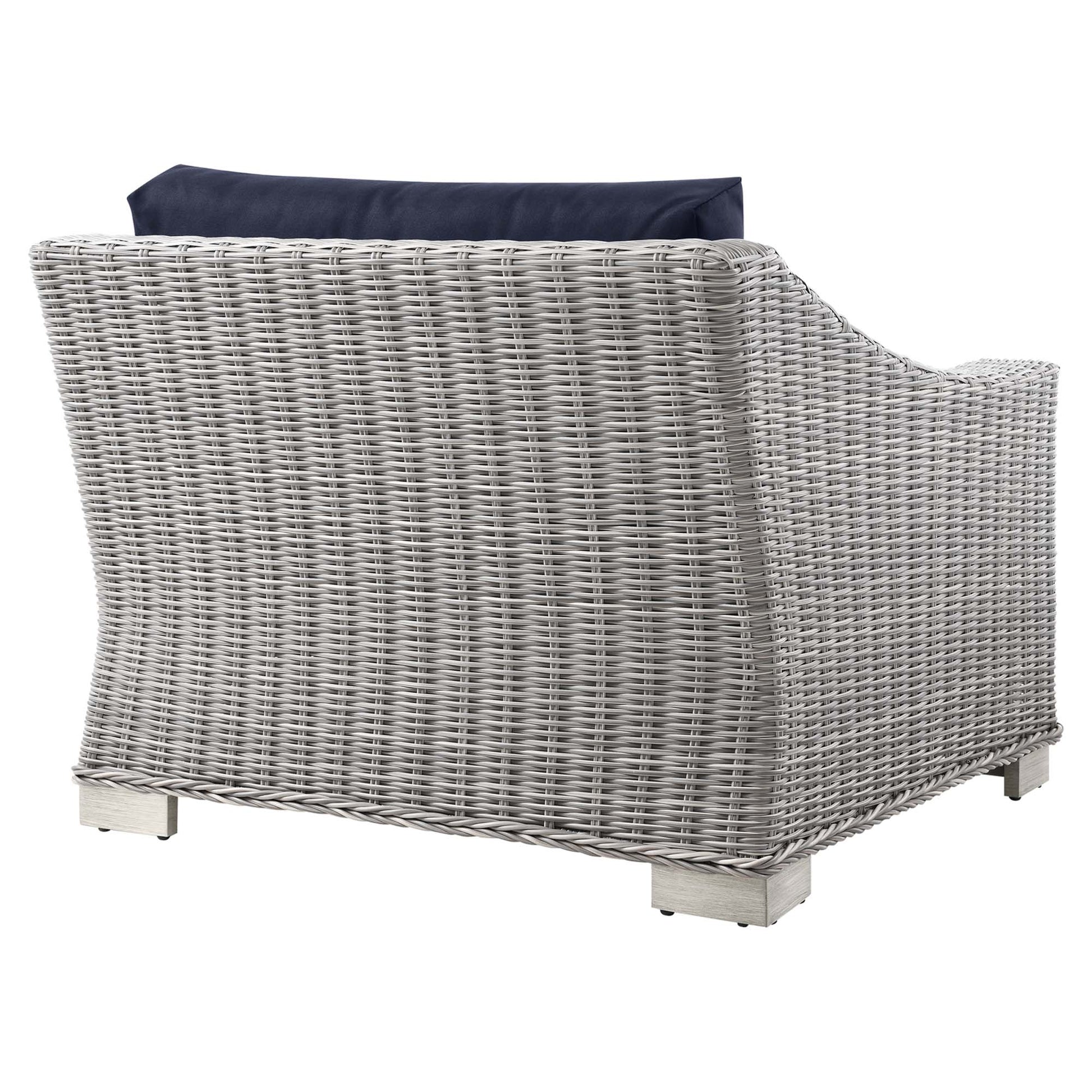 Light gray wicker outdoor armchair with navy cushion, curved arms and square block feet.