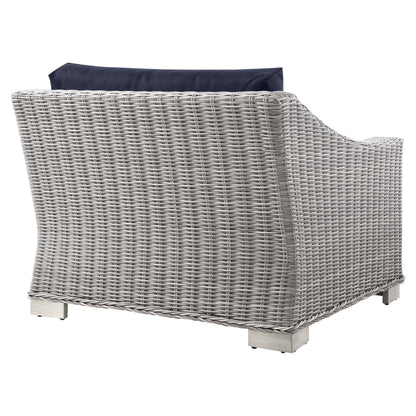 Light gray wicker outdoor armchair with navy cushion, curved arms and square block feet.