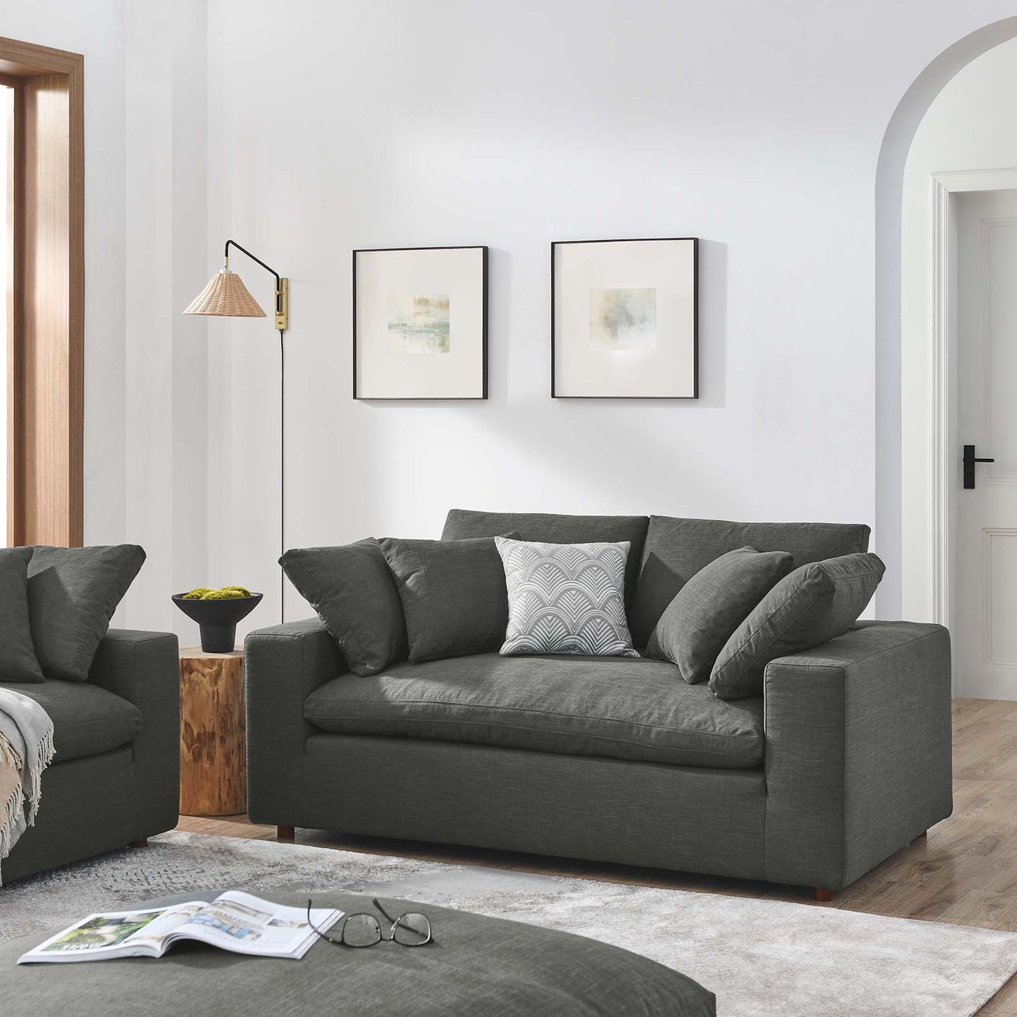 Dark gray fabric loveseat with cushions in a modern living room; woven-lamp floor light, wood stump side table, abstract wall art