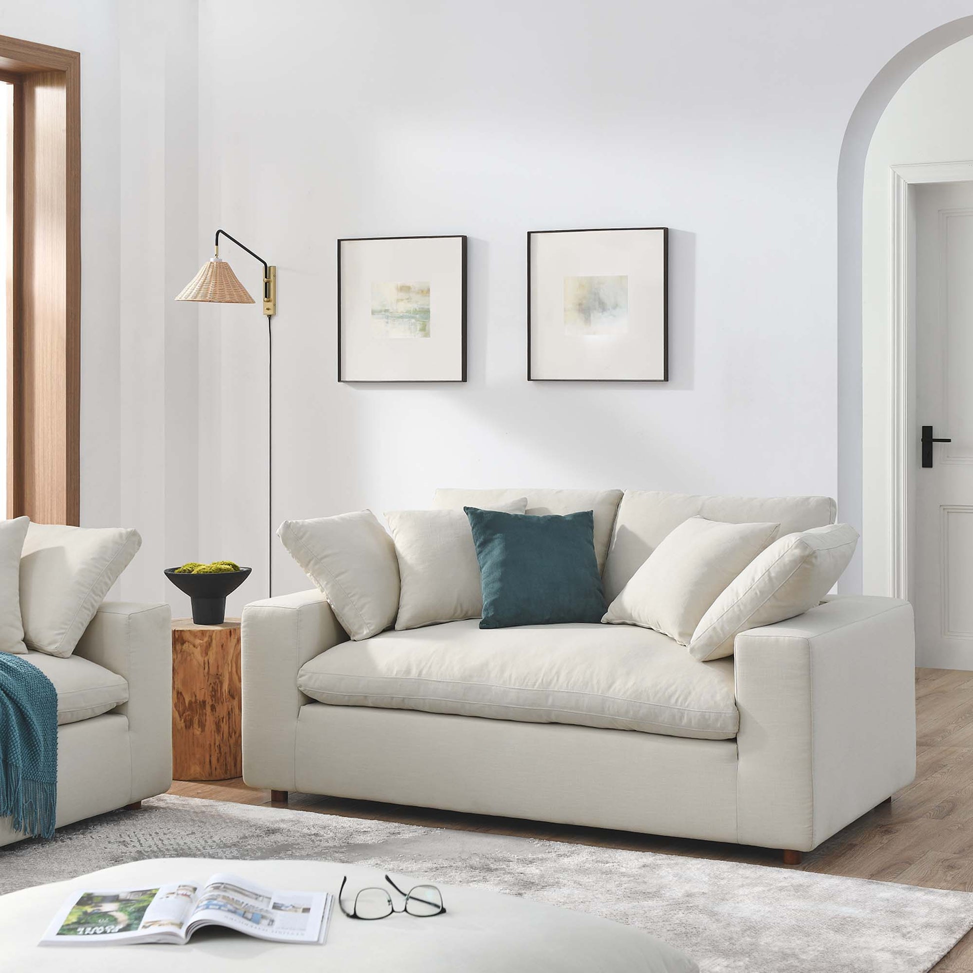 Beige modern loveseat with teal accent cushion in bright living room; two framed prints, wood stump side table, arch doorway.