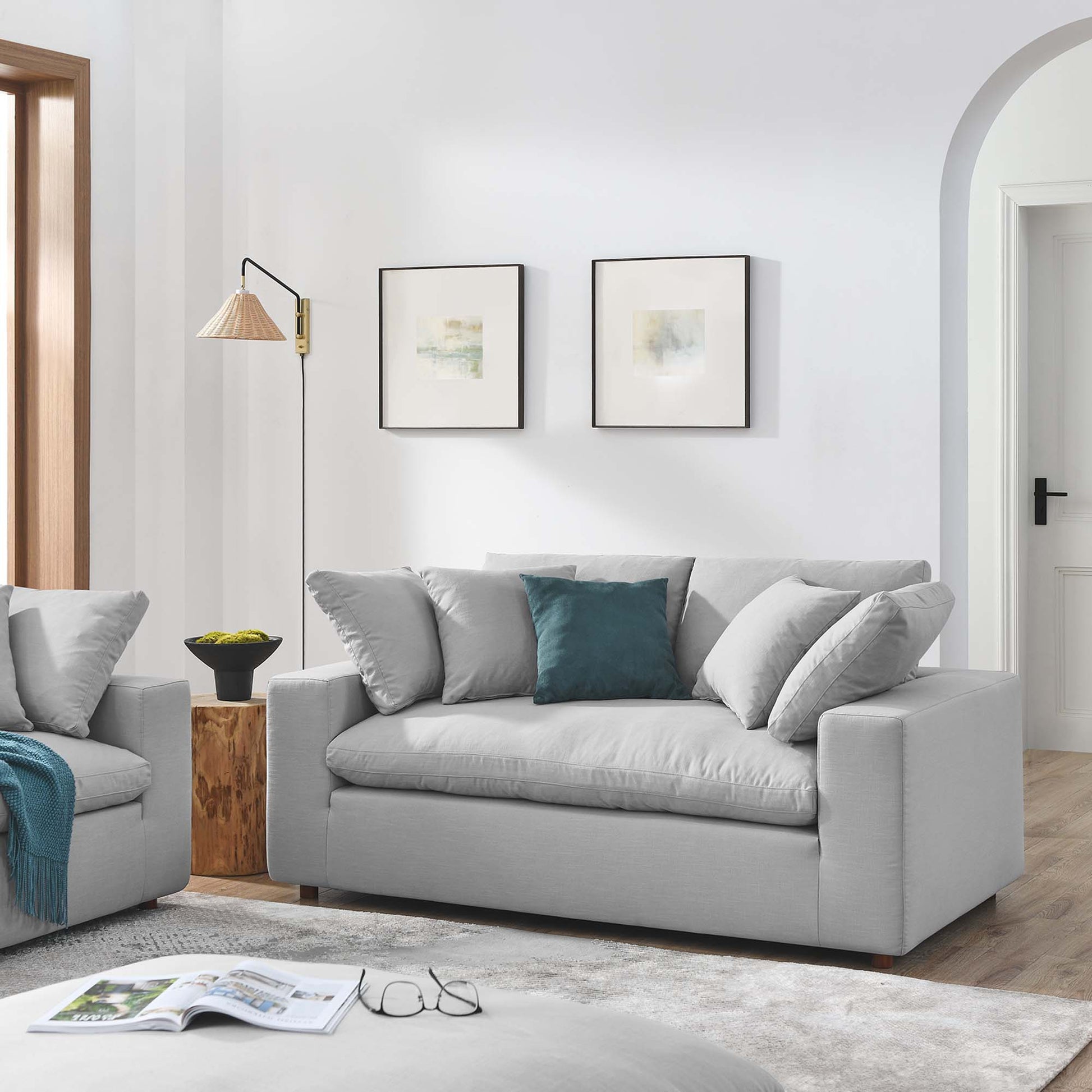 Light gray fabric loveseat with teal throw pillow in a modern living room with a wooden side table, floor lamp, and framed abstract art.