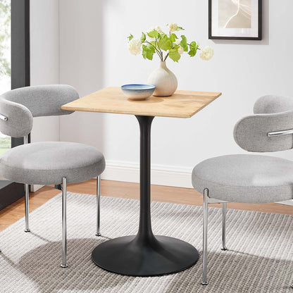 Natural wood square-top dining table on a black tulip pedestal, with two grey upholstered chairs; vase of white flowers and blue bowl.
