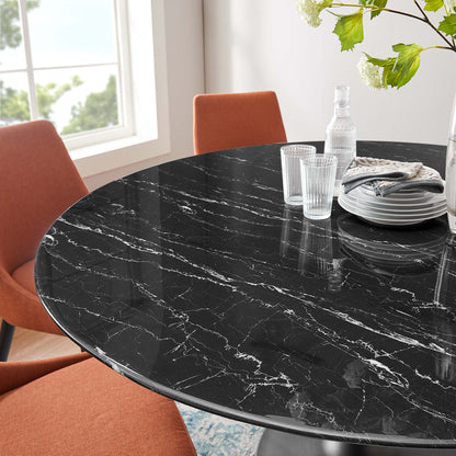 Round black faux-marble dining table with white veining, orange chairs, glassware & stacked plates in a bright dining area.