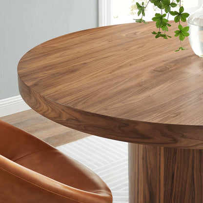 Round walnut wood dining table with a thick pedestal base; warm grain and modern rustic style.