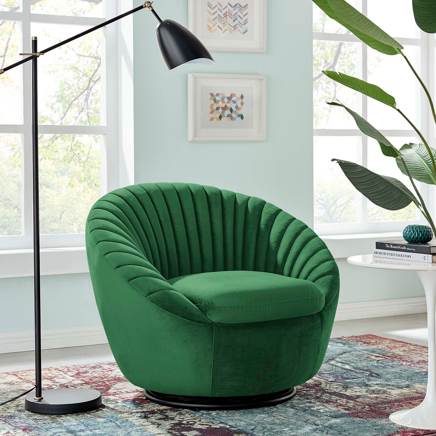 Emerald green velvet swivel lounge chair with deep channel tufting on a black circular base in a bright living room with plant and framed art.