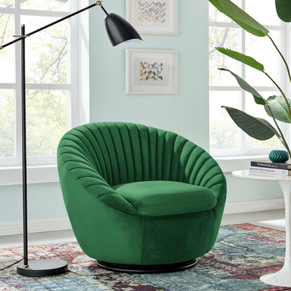 Emerald green velvet swivel lounge chair with deep channel tufting on a black circular base in a bright living room with plant and framed art.