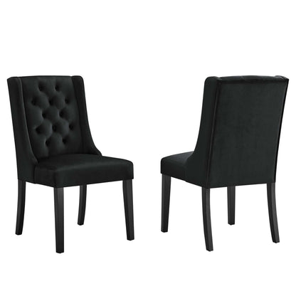 Pair of black tufted velvet dining chairs with tall curved backs & dark wooden legs.