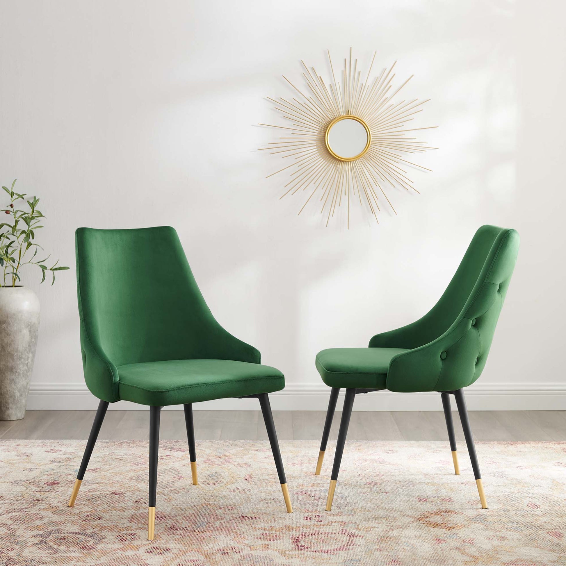 Pair of emerald green velvet dining side chairs with black legs and gold tips, set against a sunburst mirror.