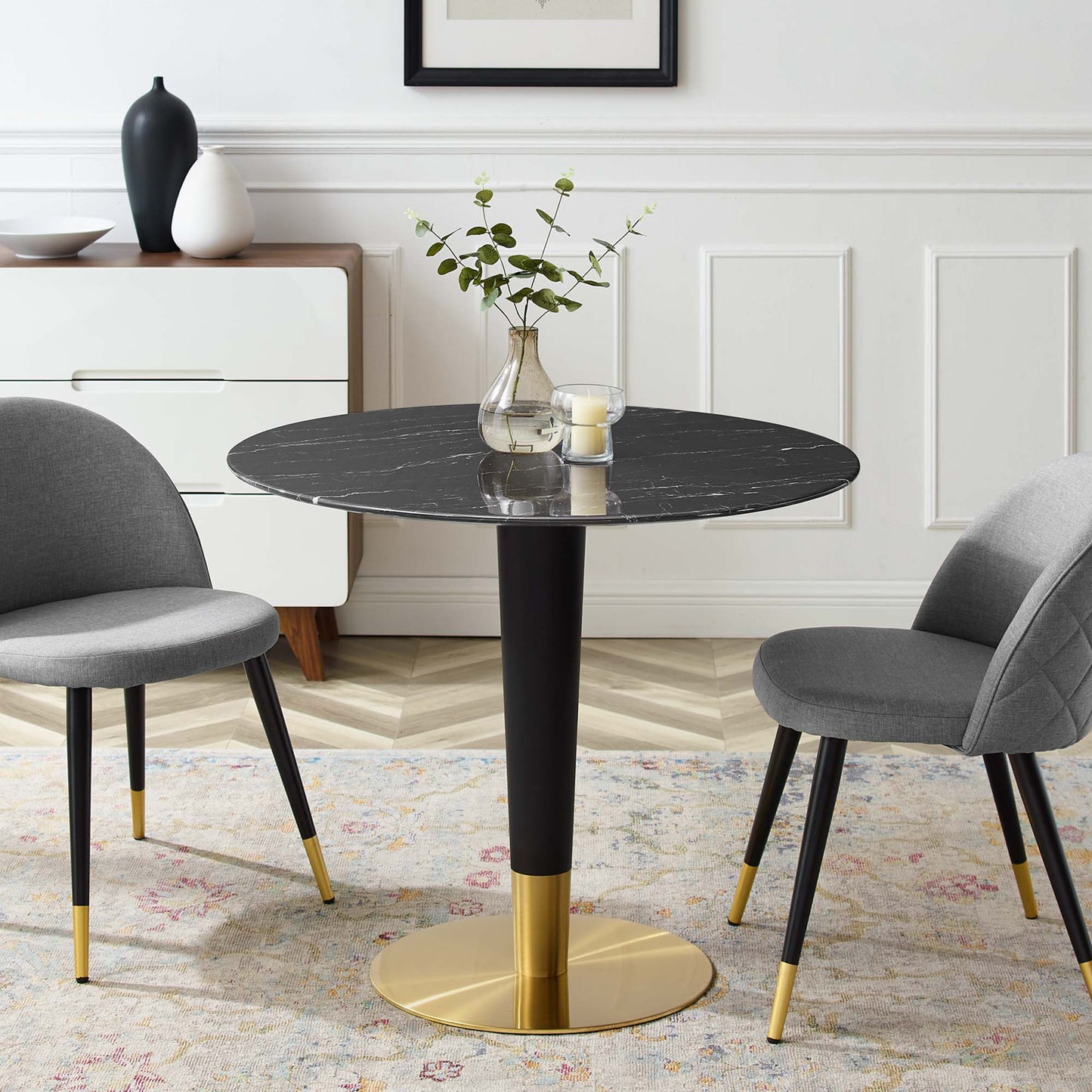 Round black artificial marble dining table with a gold pedestal base, paired with gray upholstered chairs with gold-tipped legs.