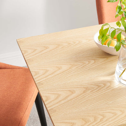 Light maple wood table top with visible grain, orange upholstered chair, white bowl with green plant, glass with straw.
