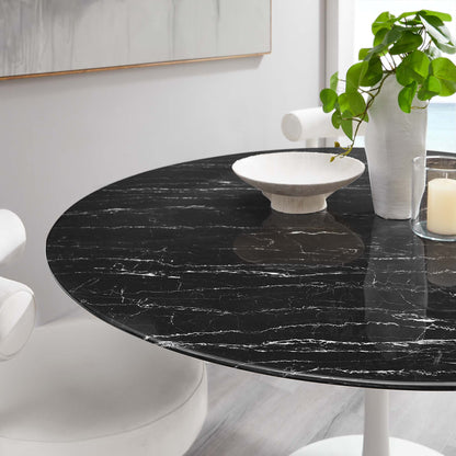 Round black faux marble-top dining table with white pedestal base, plant, bowl and candle decor.