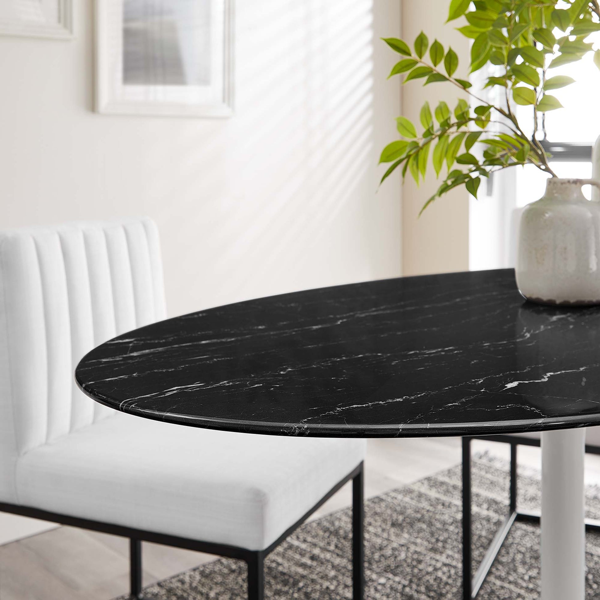 Oval black marble-look dining table with white veining on metal legs in a bright modern dining nook with a potted plant.