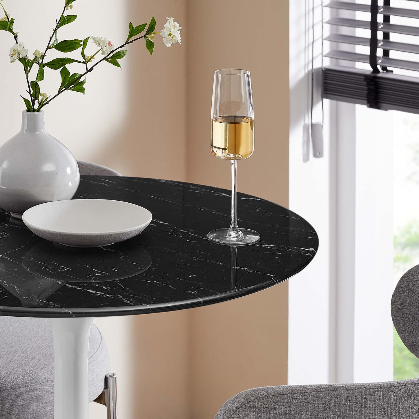 Round black faux marble bar table with white veining, a vase of white flowers, a white plate, and a champagne glass.