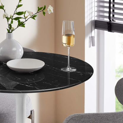 Round black faux marble bar table with white veining, a vase of white flowers, a white plate, and a champagne glass.