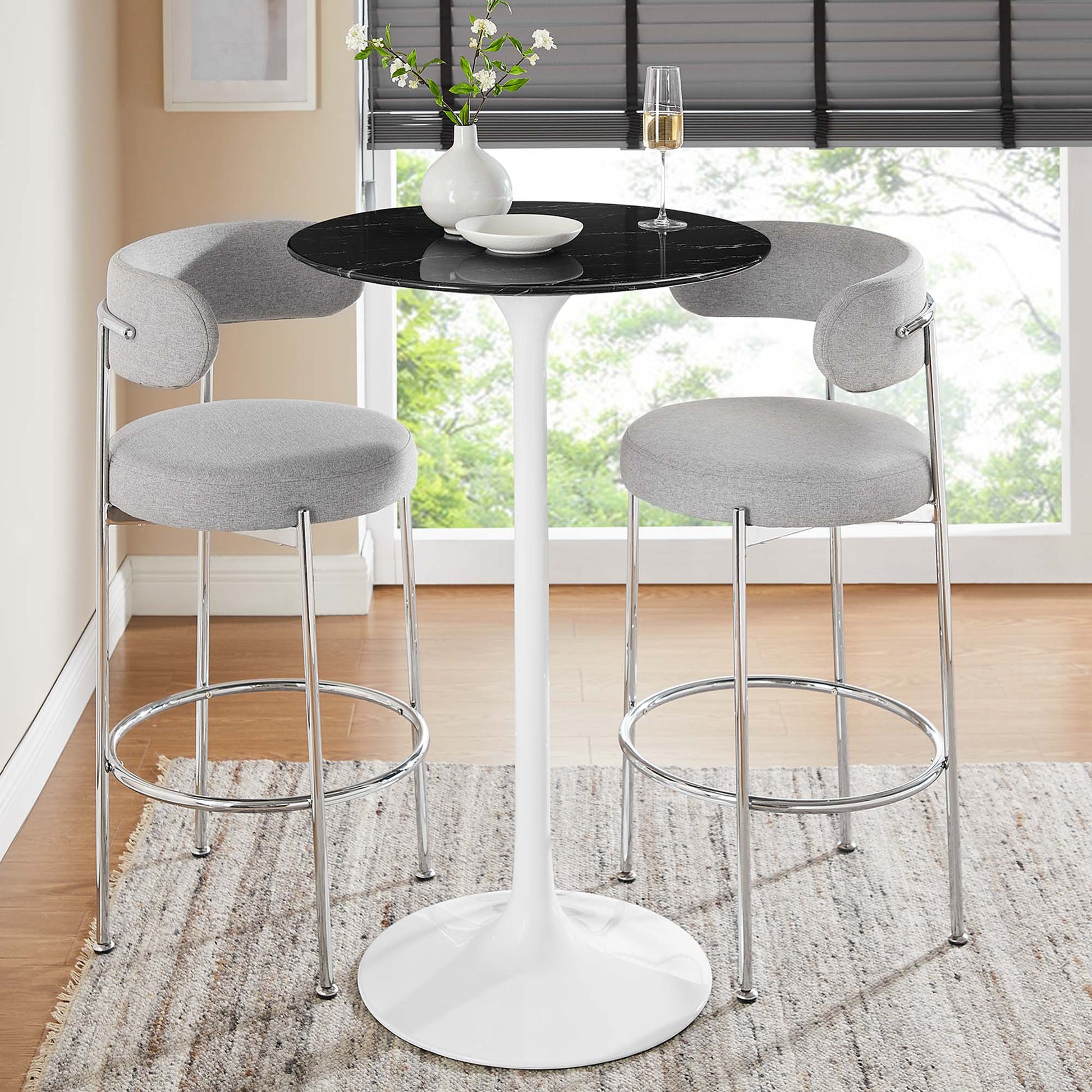 Modern white tulip pedestal table with black glass top, two gray upholstered bar stools with chrome frames and footrests.