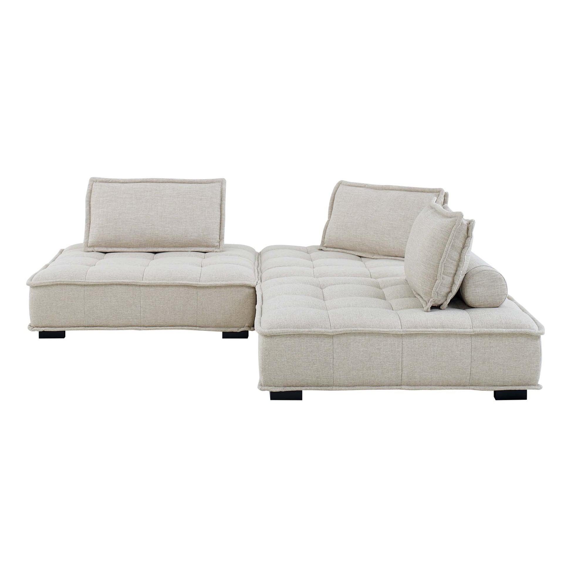 Beige fabric L-shaped sectional with tufted cushions, chaise on the right, multiple back pillows, low black legs.