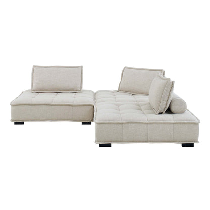 Beige fabric L-shaped sectional with tufted cushions, chaise on the right, multiple back pillows, low black legs.