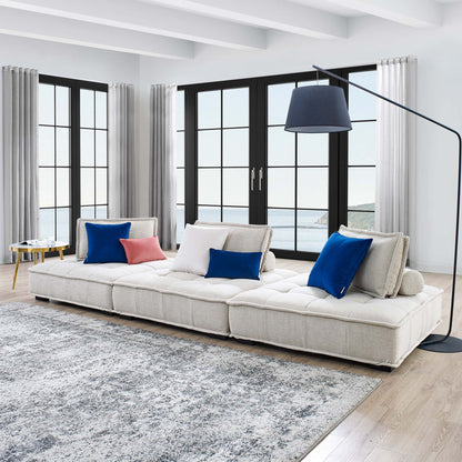 Beige tufted modular sofa with blue and peach cushions in bright living room with black-framed windows and arc floor lamp.