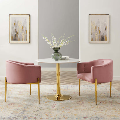 Pink velvet accent chairs with gold legs sit around a round white table with a gold pedestal base, vase of white flowers.