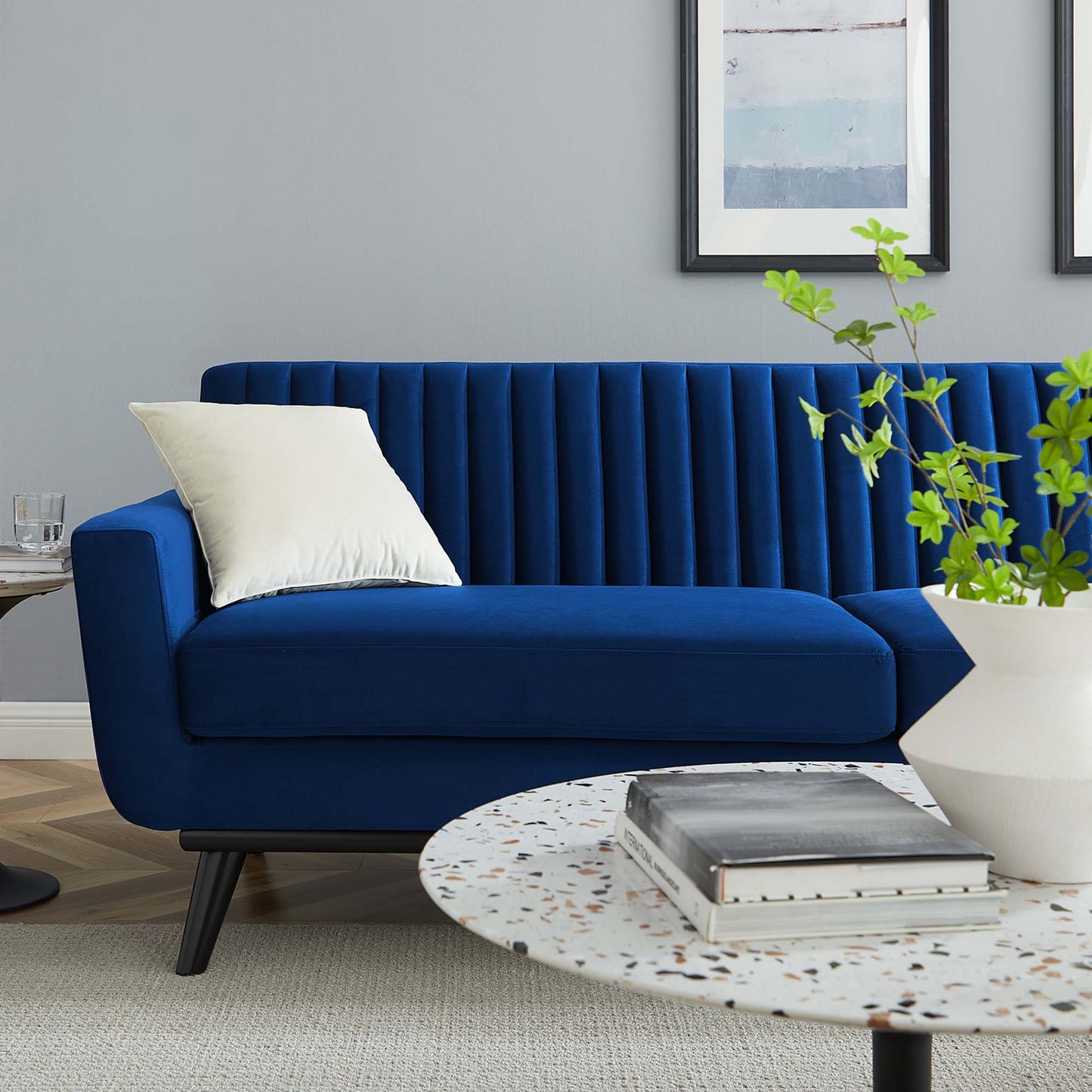 Navy blue velvet sofa with vertical channel tufting, white cushion, terrazzo round coffee table, plant in white pot.