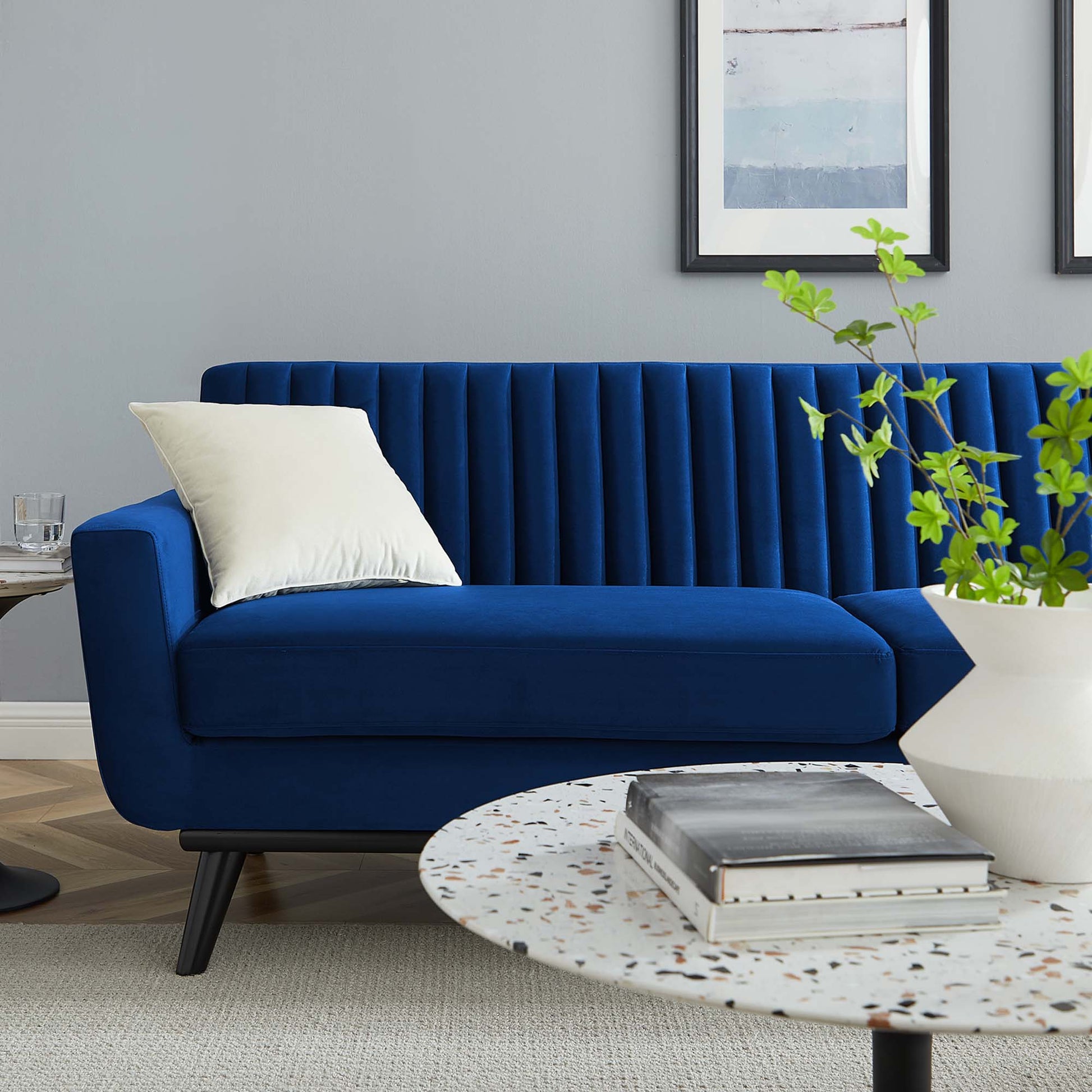 Navy blue velvet sofa with vertical channel tufting, white cushion, terrazzo round coffee table, plant in white pot.