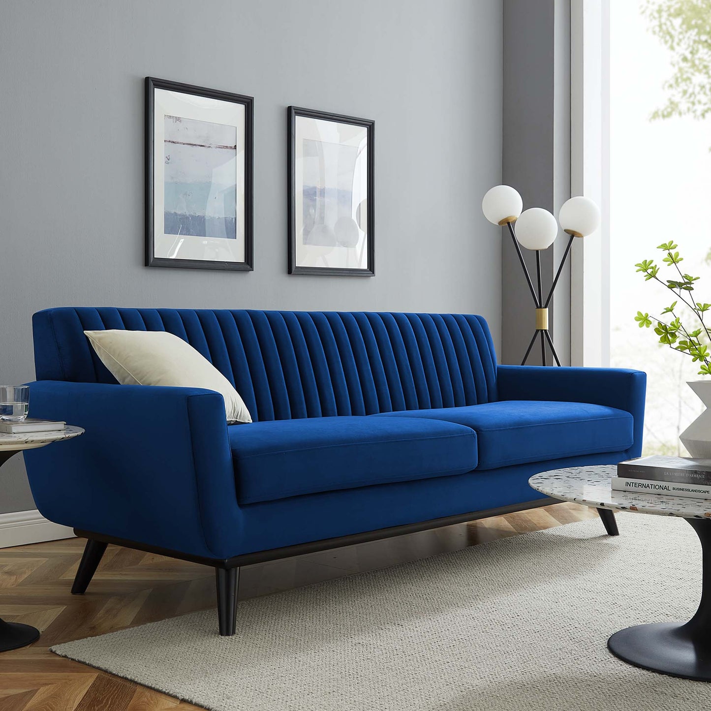 Navy blue velvet sofa with vertical channel tufting, black legs, cream pillow.