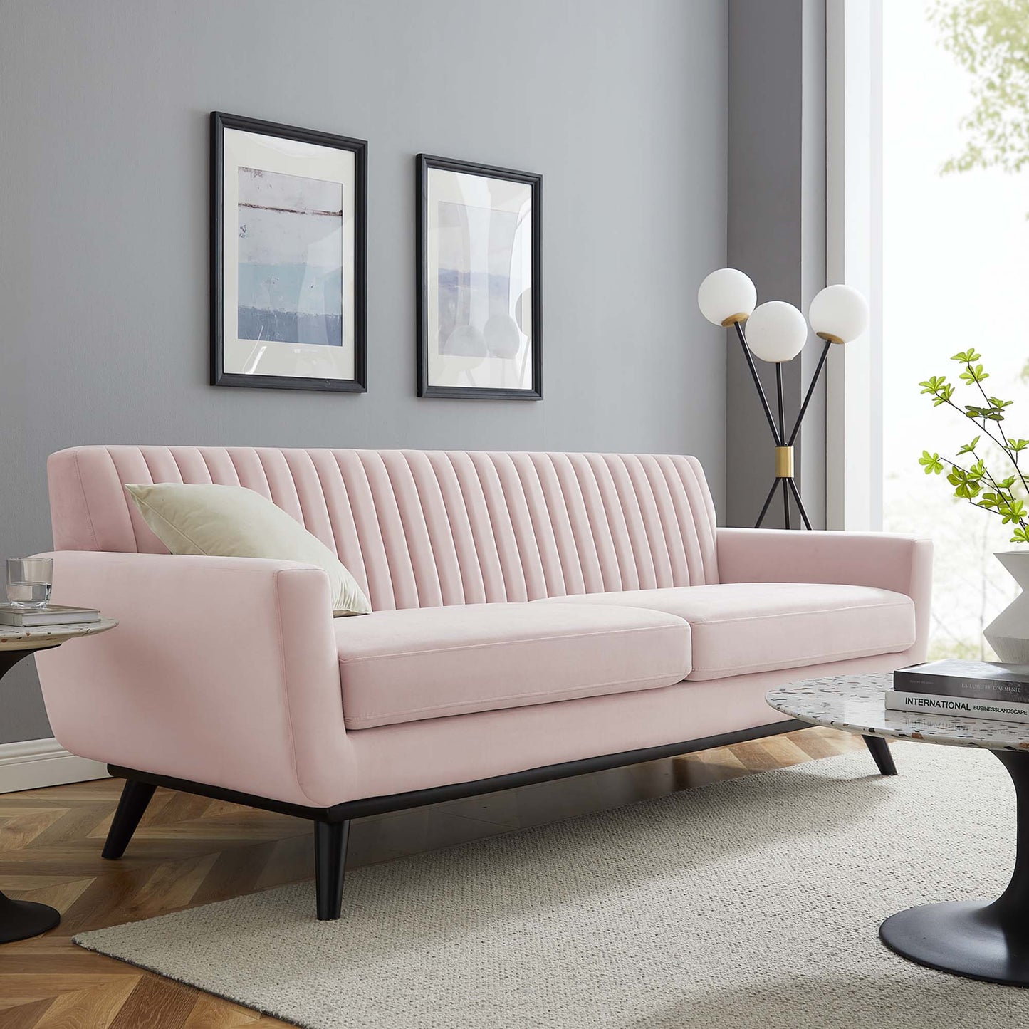 Pastel pink velvet mid-century modern sofa with vertical channel tufting and black angled legs.