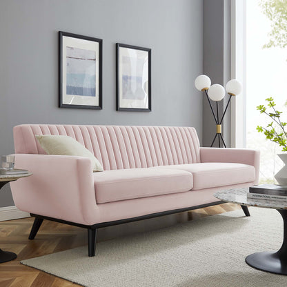 Pastel pink velvet mid-century modern sofa with vertical channel tufting and black angled legs.