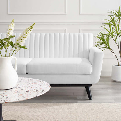 White mid-century loveseat with vertical channeling and black legs in a bright living room with a round terrazzo coffee table.