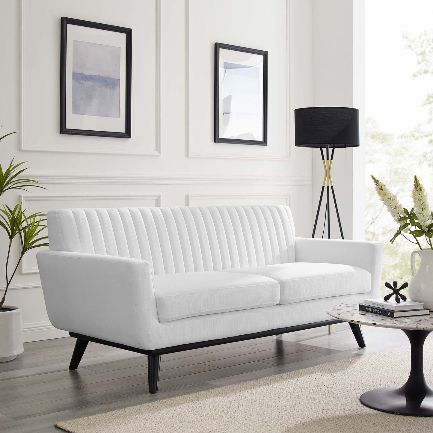 White fabric loveseat with vertical channel tufting and black tapered legs in a bright modern living room.