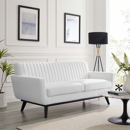 White fabric loveseat with vertical channel tufting and black tapered legs in a bright modern living room.
