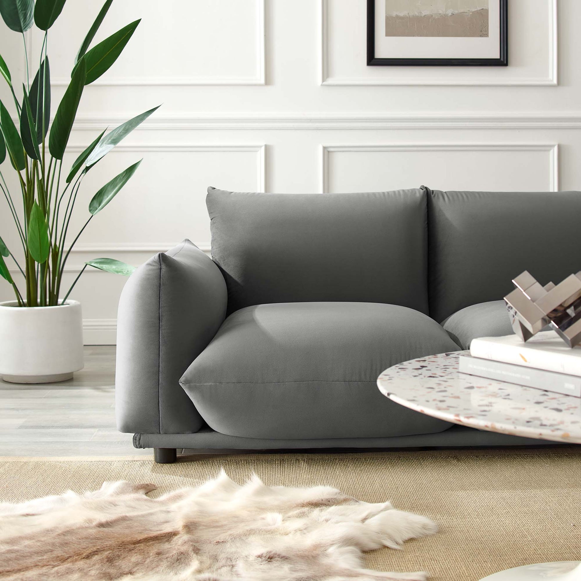 Gray velvet loveseat with rounded arms in a white-paneled living room, with a round terrazzo coffee table.