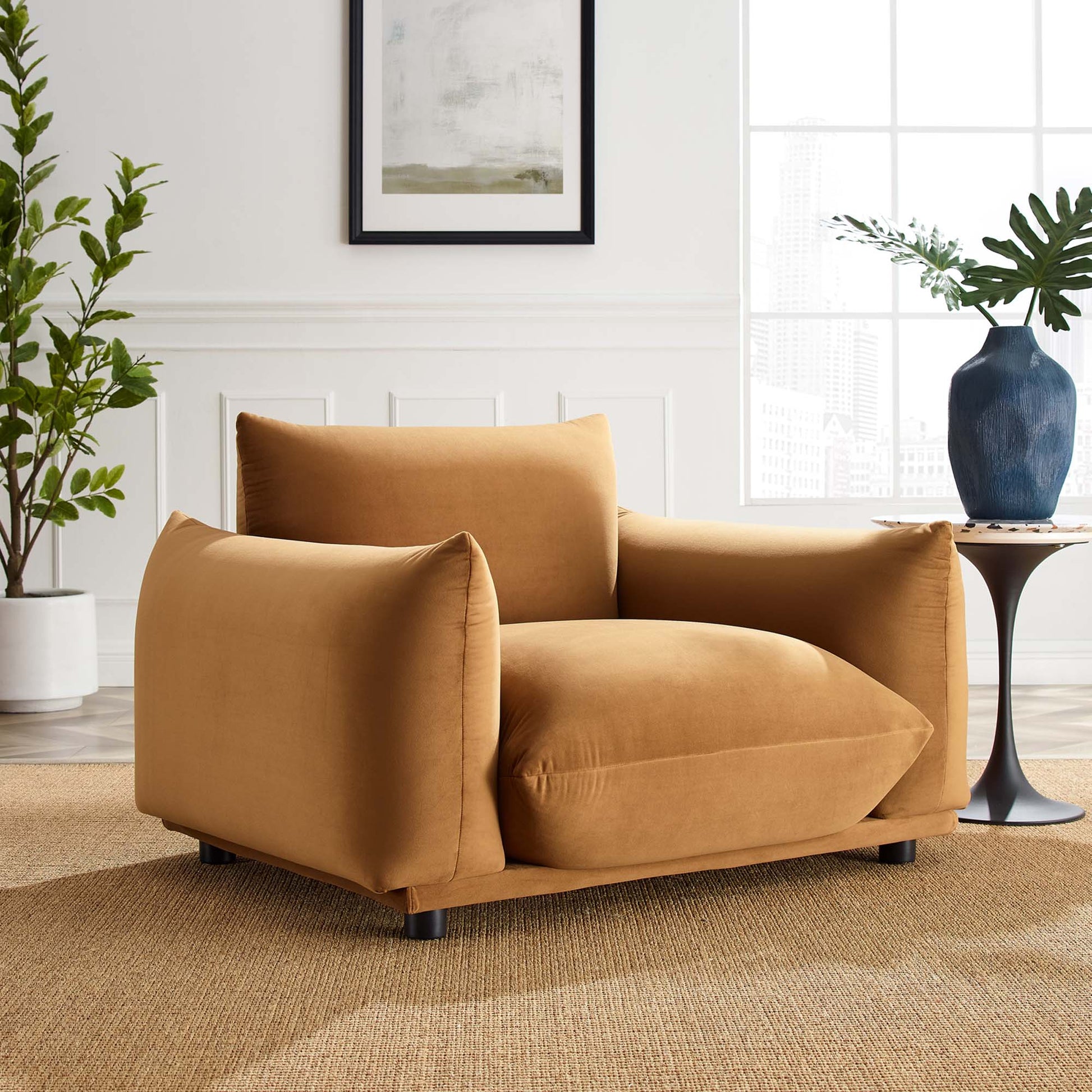 Cognac-colored velvet armchair with wide rounded arms, back cushions & dark short legs in a bright living room.