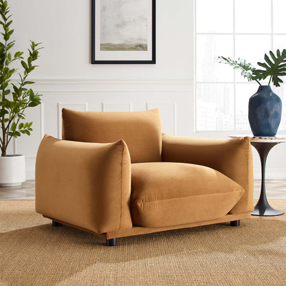 Cognac-colored velvet armchair with wide rounded arms, back cushions & dark short legs in a bright living room.