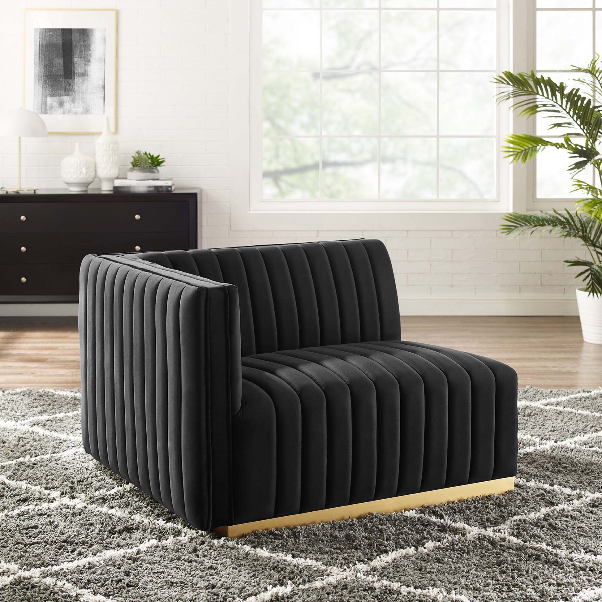 Black velvet channel-tufted lounge chair with a gold-tone base in a bright modern living room.