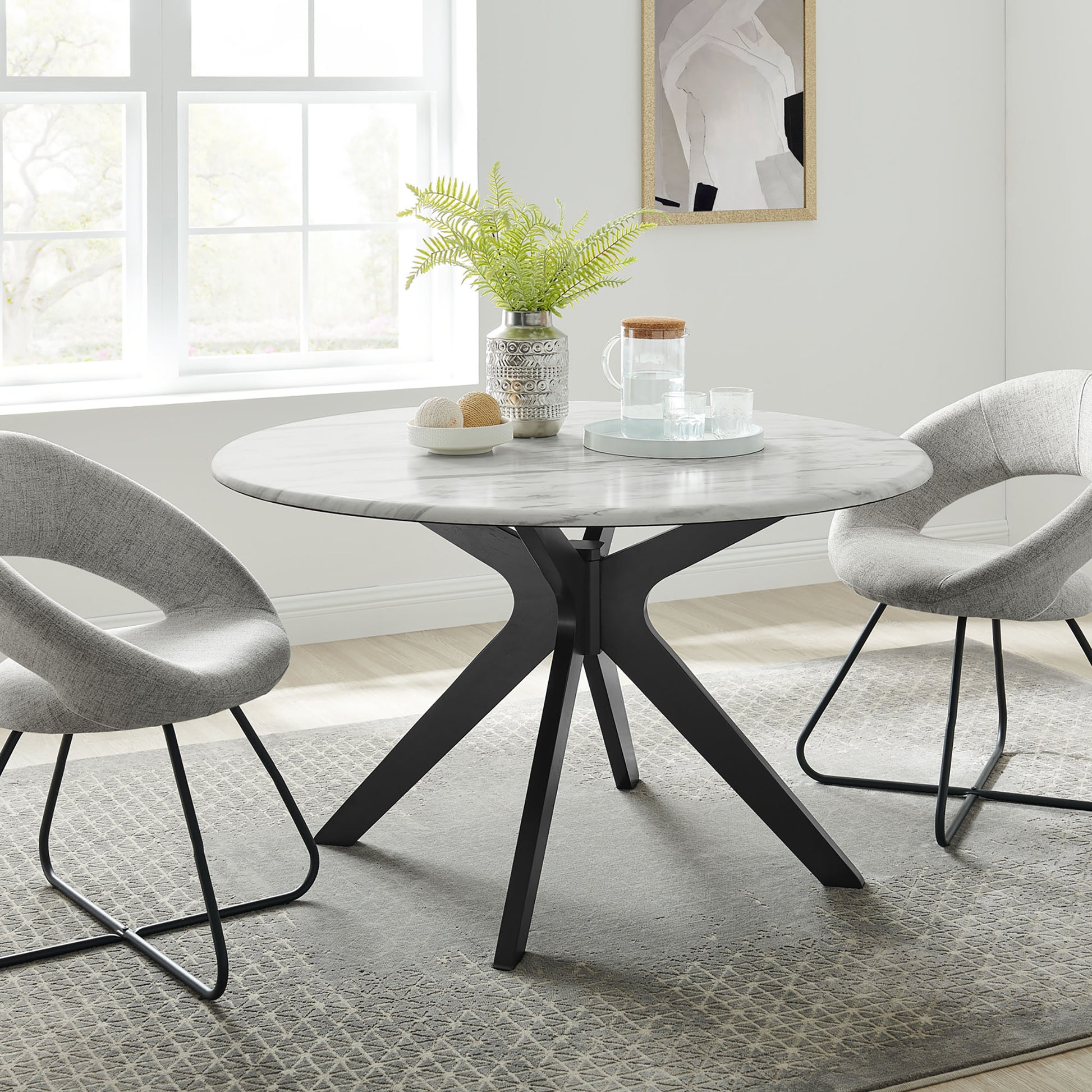 Round marble-top dining table with a black angular pedestal base, paired with gray upholstered chairs and a fern centerpiece.