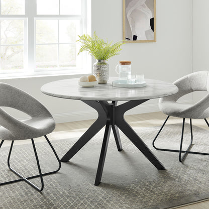 Round marble-top dining table with a black angular pedestal base, paired with gray upholstered chairs and a fern centerpiece.