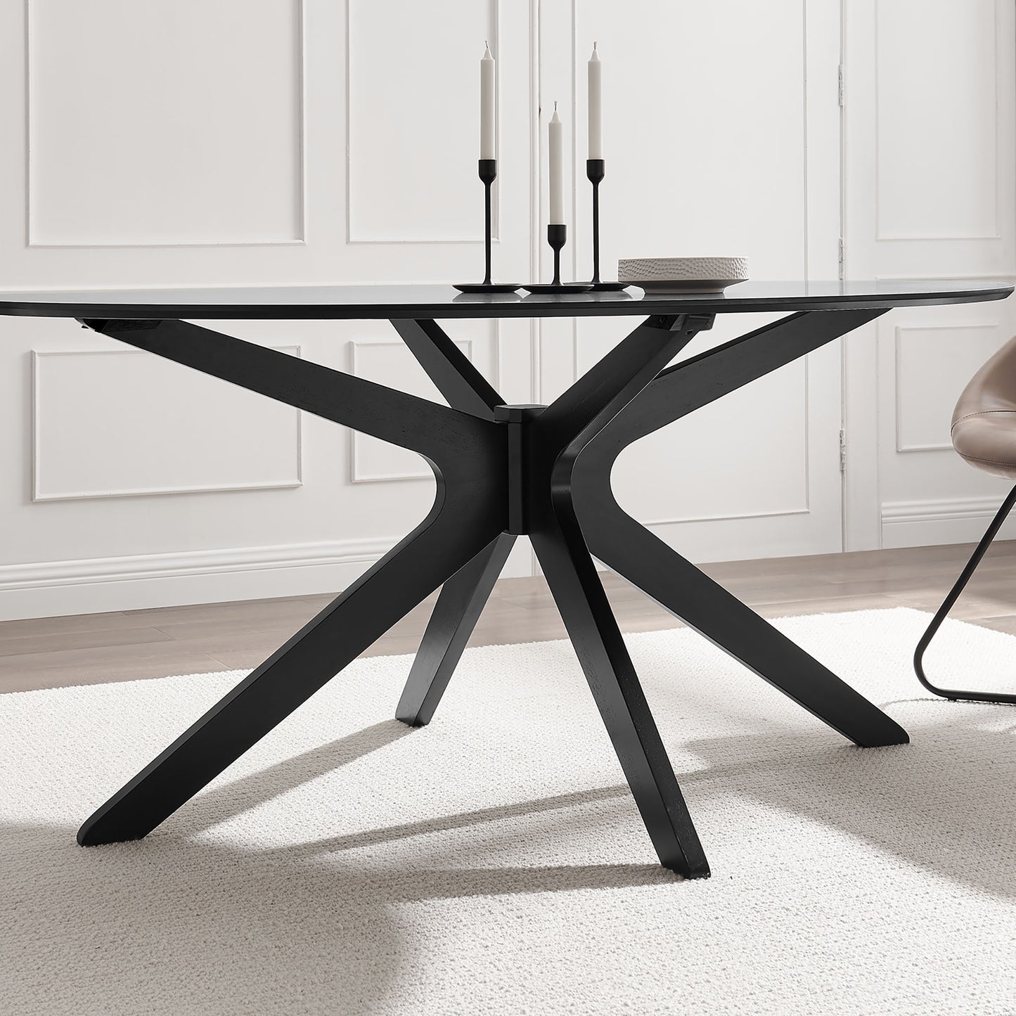 Black glass-top dining table with sculptural X-shaped pedestal base.