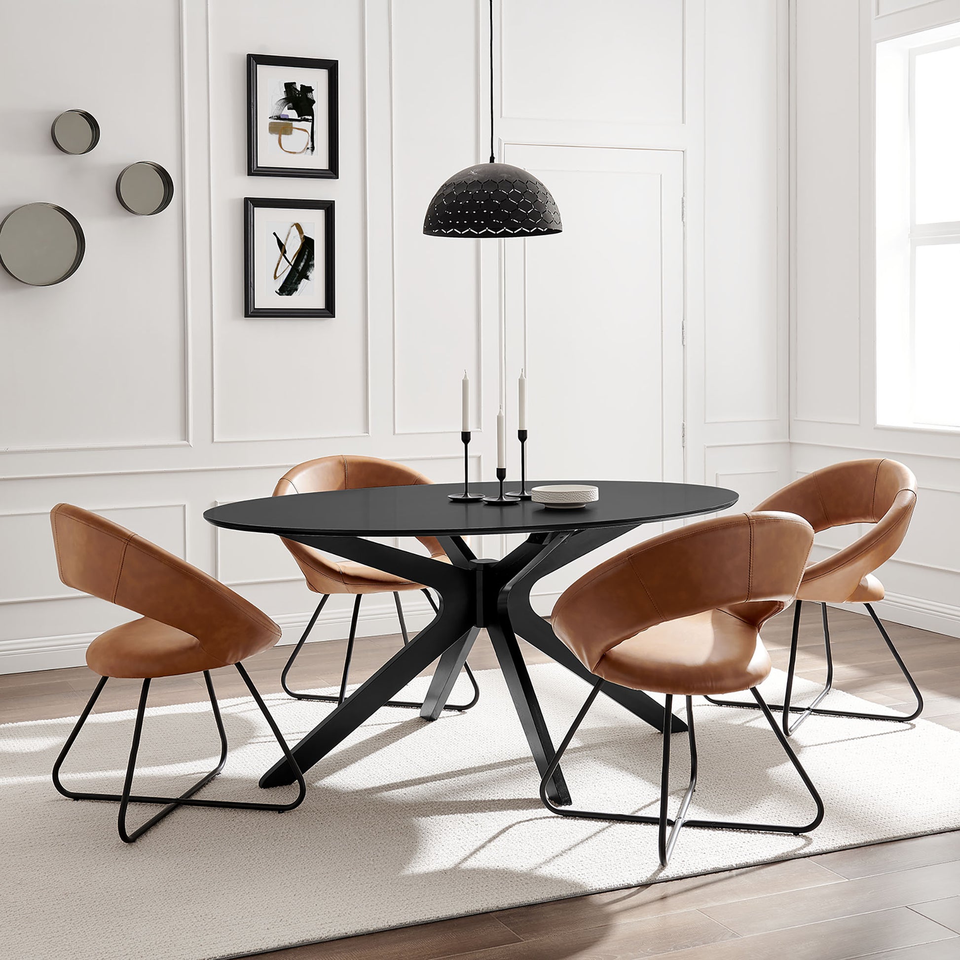 Black oval dining table with an X-shaped metal base, tan leather chairs, pendant lamp, white paneled walls