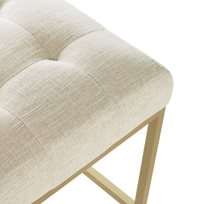Beige linen-tufted stool with light gold wooden legs, rectangular modern glam seating.