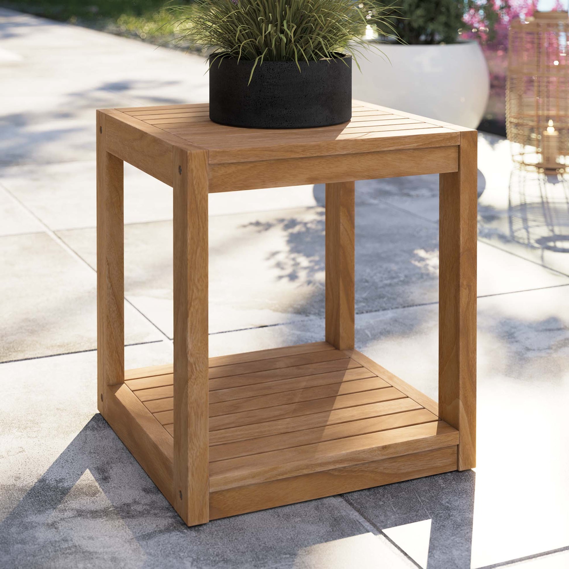 Natural wood outdoor cube side table with a slatted lower shelf, green plant in black pot on top.
